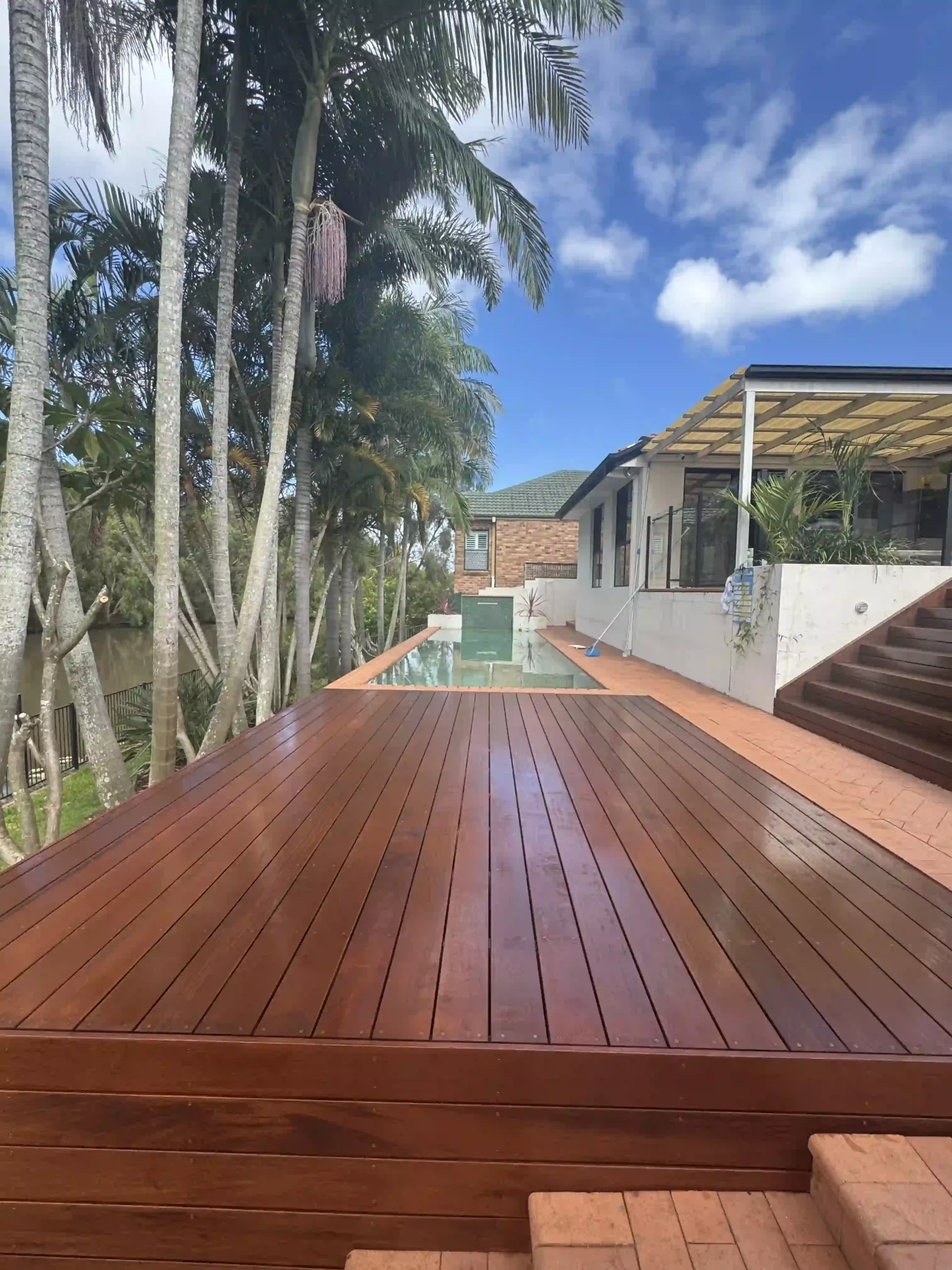 A hardwood deck beside a pool, framed by palms, built for coastal living